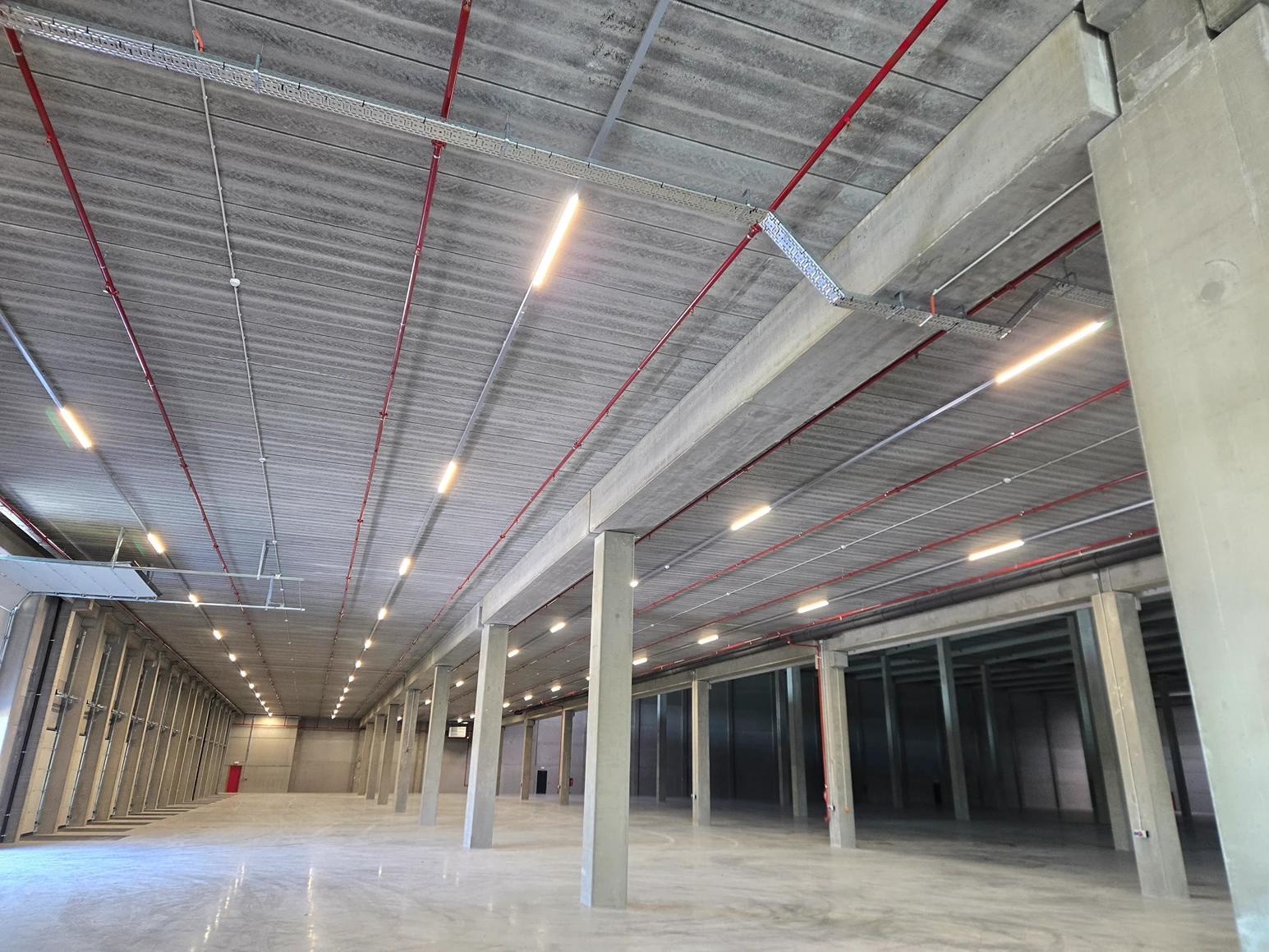 Logistieke hal met betonnen kolommen en ledverlichting, beveiligd met optische branddetectie en airsampling
